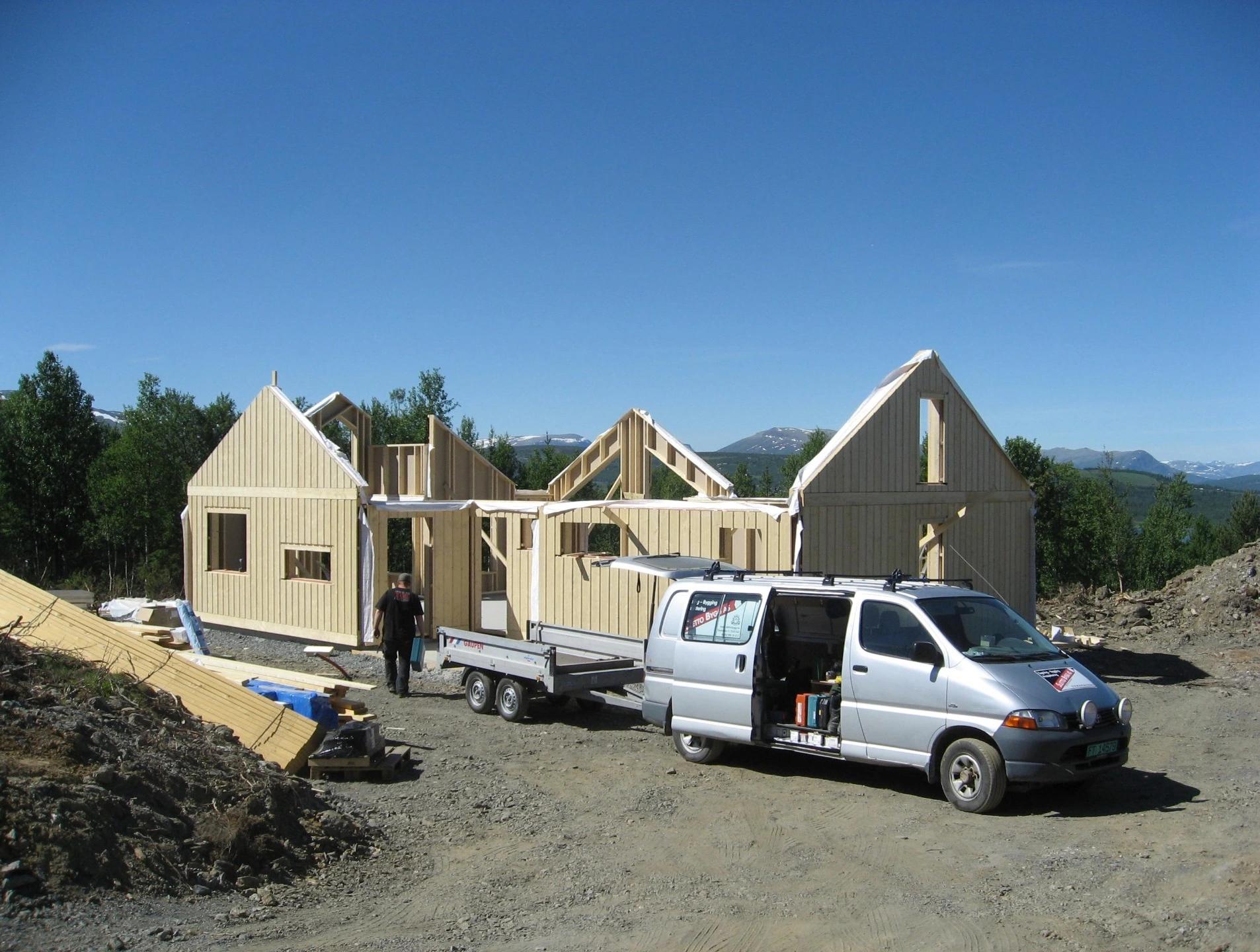 A cabin frame going up on site, with a van and trailer of timber in front