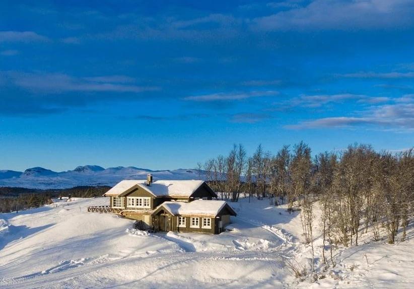 Two dark cabins in snow on an open fell, mountains behind