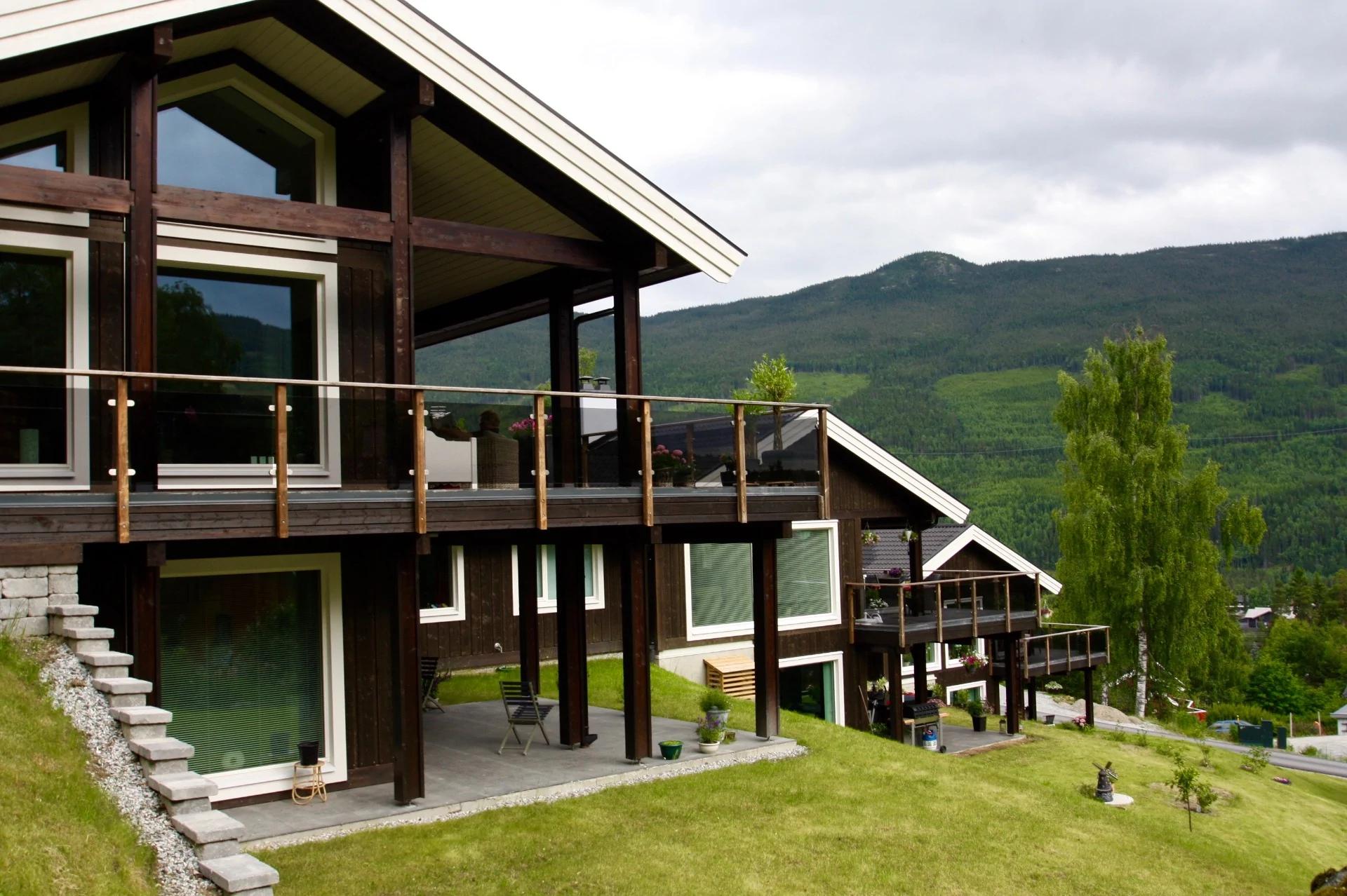 A dark-stained house with a wide balcony on a green hillside