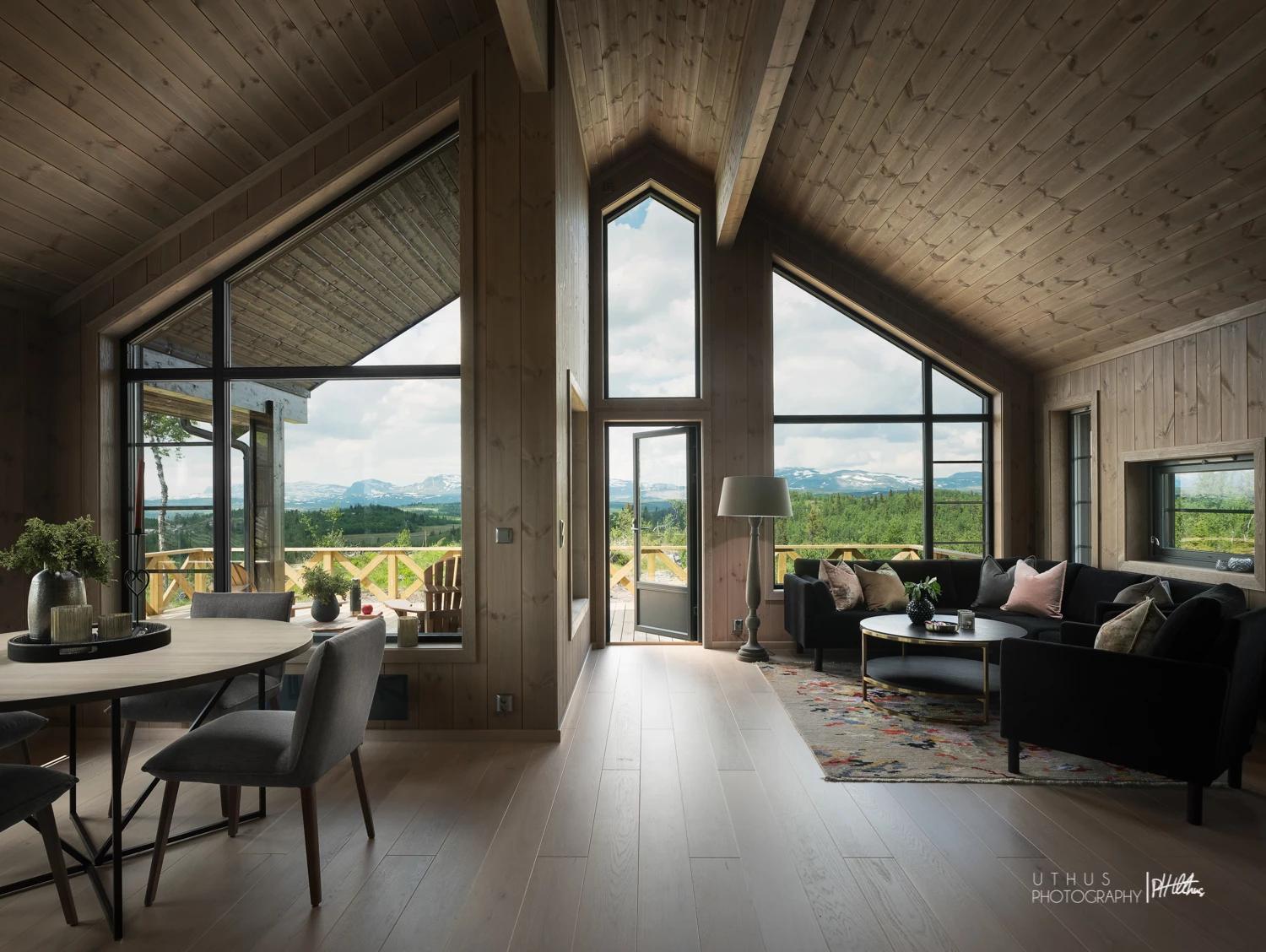 A cabin living room under a high wooden ceiling, with tall windows to the view