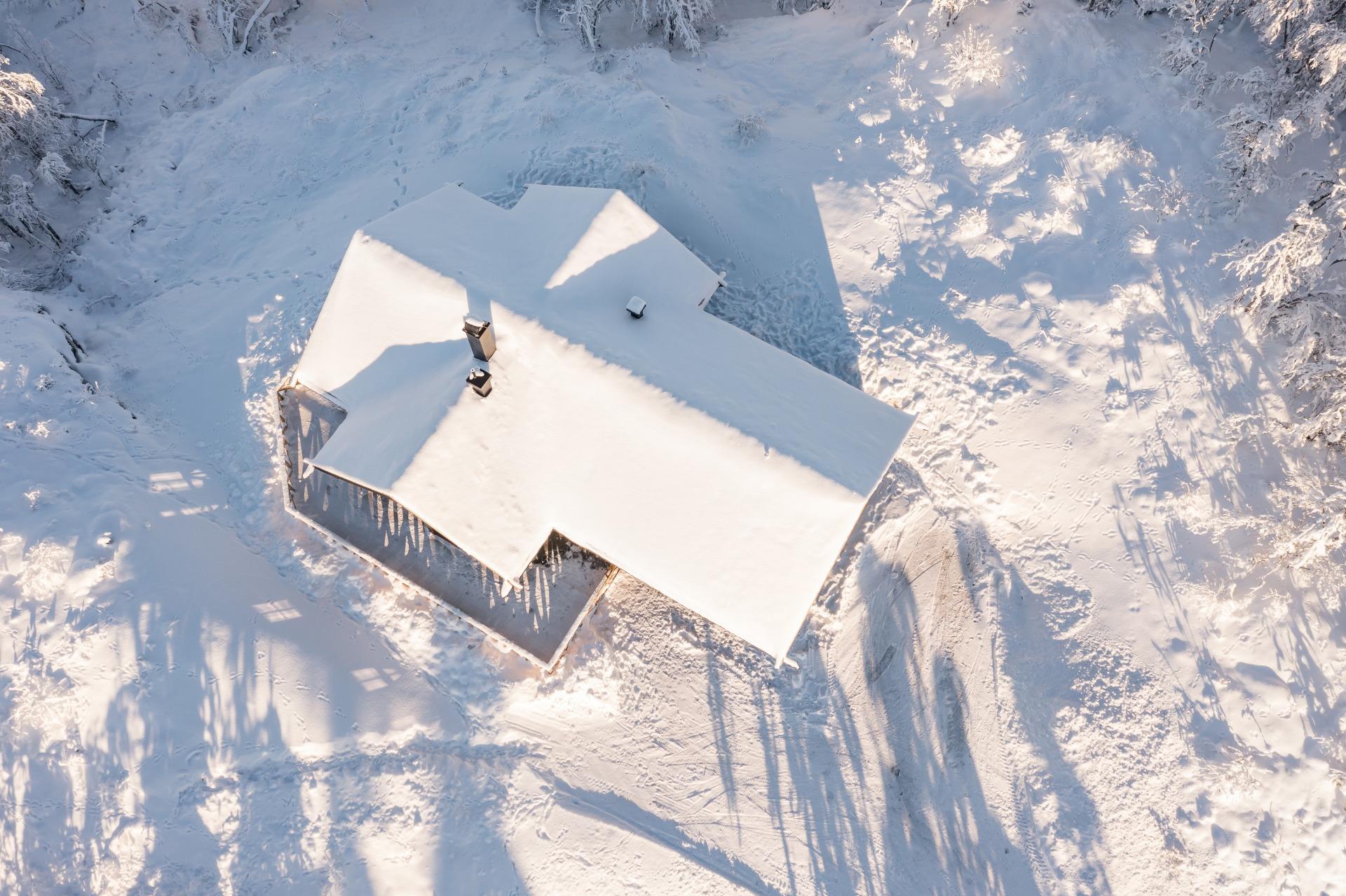 The cabin seen from above, its roof deep in snow