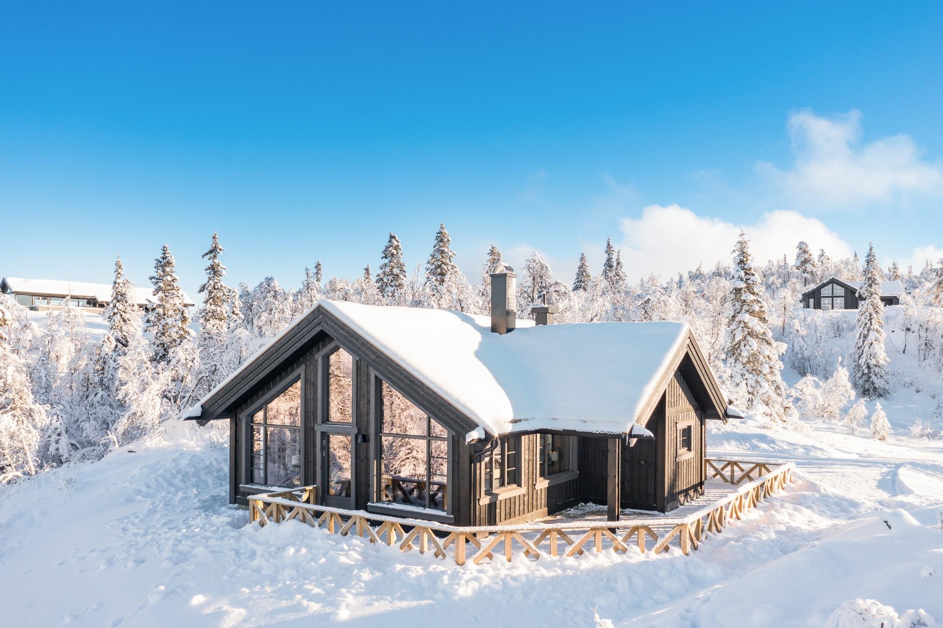The new cabin from the front: dark walls, tall windows and a terrace fence, in snow