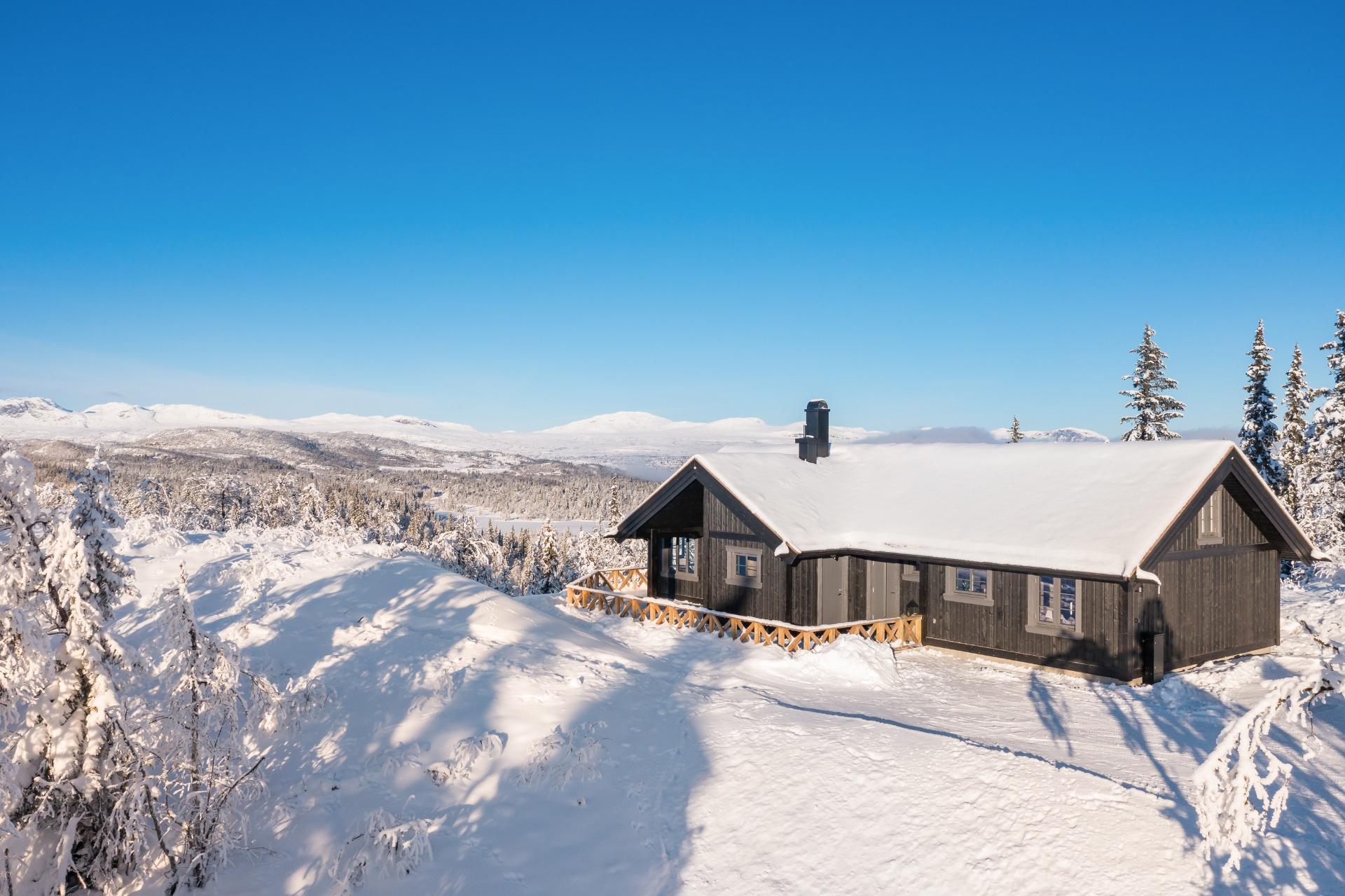 The cabin on its ridge with snowy mountains along the horizon